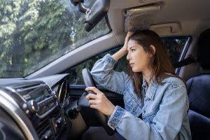 Woman putting her hand to her forward in a car.