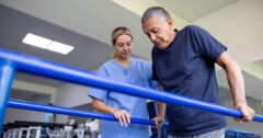 Latin American man doing physical therapy and walking holding handbars and guided by a physical therapist