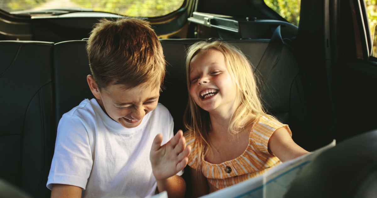 Children in a car backseat laughing.