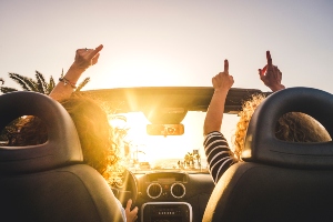 People in a car driving with their hands up.