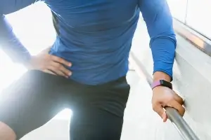 partial image of a fit 30-ish white man in a blue rash guard and biker shorts holding his hip in pain.